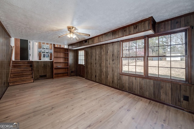 unfurnished room featuring ceiling fan, stairway, wood walls, light wood-style floors, and a textured ceiling