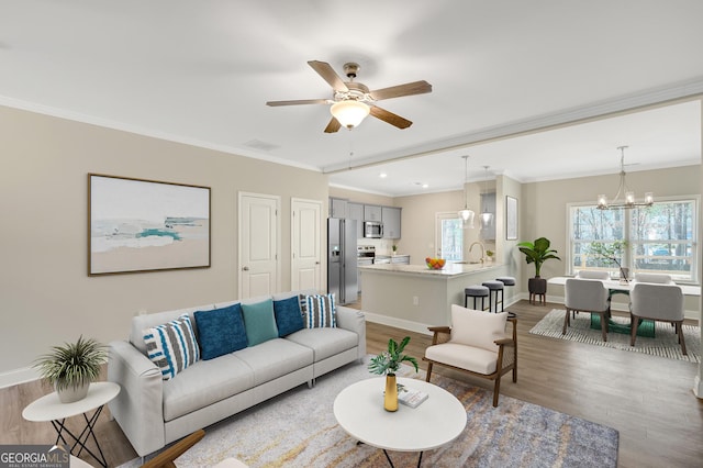 living room with hardwood / wood-style flooring, ornamental molding, sink, and ceiling fan with notable chandelier