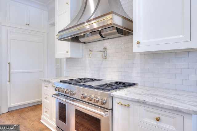 kitchen with island range hood, light stone countertops, light hardwood / wood-style floors, white cabinets, and range with two ovens