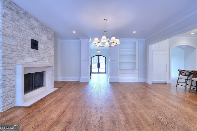 unfurnished living room with a fireplace, a chandelier, hardwood / wood-style flooring, ornamental molding, and built in shelves