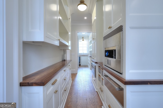 kitchen with white cabinetry, butcher block countertops, crown molding, and light hardwood / wood-style floors