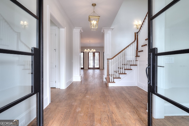 entrance foyer featuring ornate columns, wood-type flooring, a chandelier, crown molding, and french doors