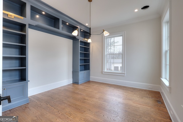 unfurnished dining area with wood-type flooring, crown molding, and built in shelves