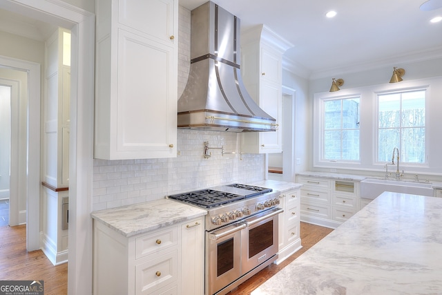 kitchen with sink, white cabinets, double oven range, light stone countertops, and wall chimney range hood