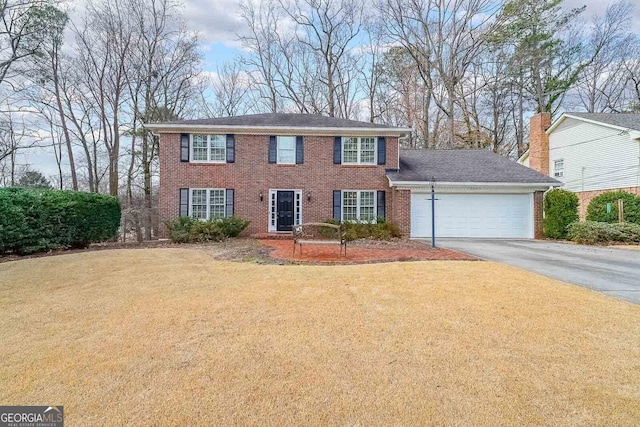 colonial home with driveway, an attached garage, a front lawn, and brick siding