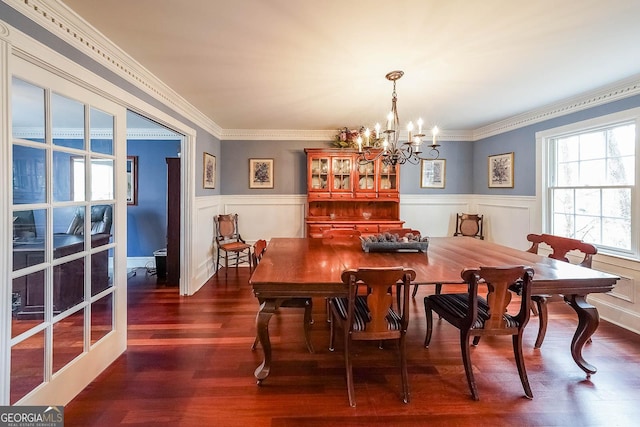 dining space with dark wood-style floors, a wainscoted wall, crown molding, and an inviting chandelier