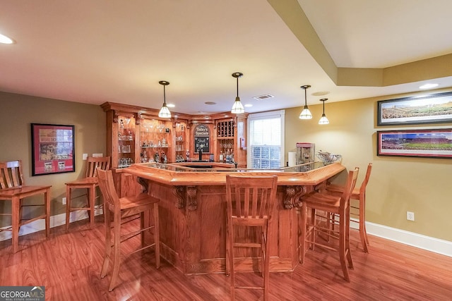 bar with baseboards, visible vents, indoor wet bar, and wood finished floors