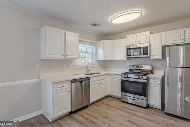 kitchen featuring sink, white cabinetry, light hardwood / wood-style flooring, a textured ceiling, and appliances with stainless steel finishes