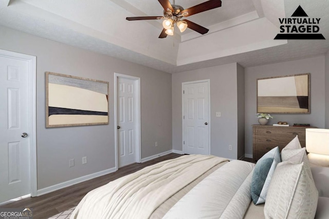 bedroom featuring a tray ceiling, dark wood-type flooring, and ceiling fan