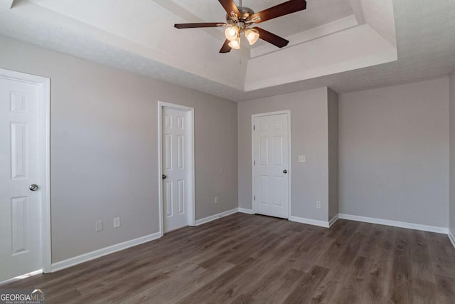 unfurnished bedroom featuring ceiling fan, dark hardwood / wood-style flooring, a raised ceiling, and a textured ceiling