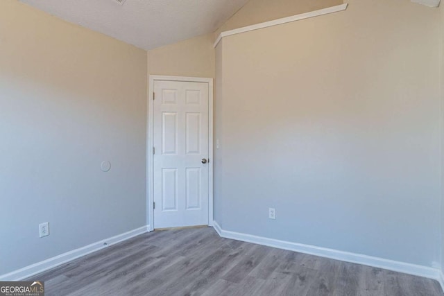 spare room featuring wood-type flooring, vaulted ceiling, and a textured ceiling