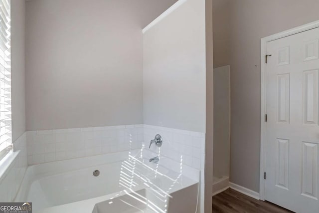 bathroom with a relaxing tiled tub and hardwood / wood-style flooring