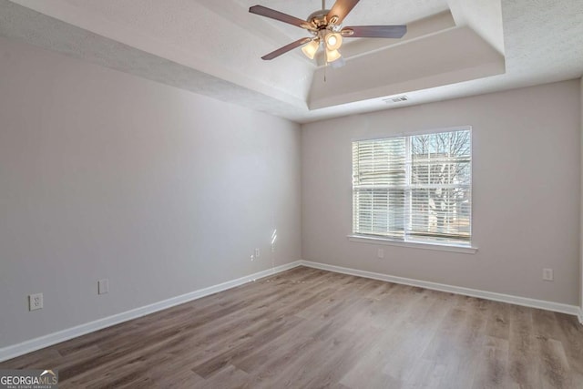 empty room with ceiling fan, a tray ceiling, and hardwood / wood-style floors