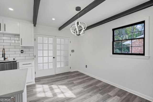 unfurnished dining area featuring a notable chandelier, beam ceiling, and light wood-type flooring