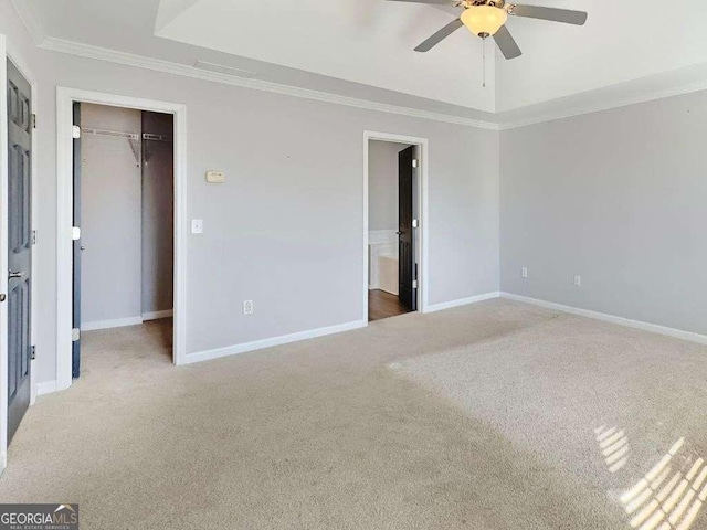 unfurnished bedroom featuring crown molding, carpet, a tray ceiling, a spacious closet, and a closet