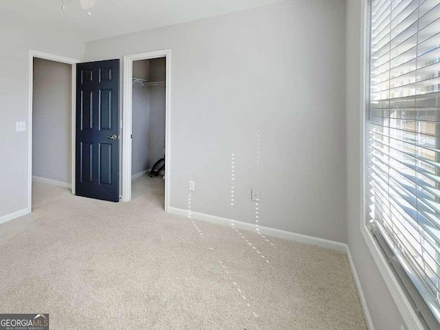 unfurnished bedroom featuring a spacious closet, light colored carpet, and a closet