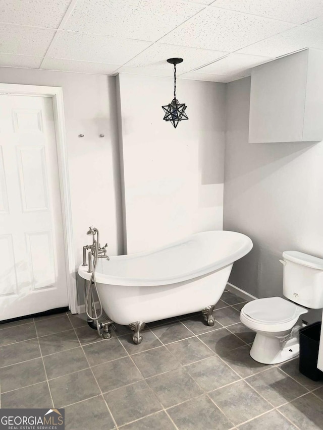 bathroom featuring a bathing tub, a paneled ceiling, tile patterned floors, and toilet