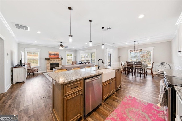 kitchen with sink, dark wood-type flooring, appliances with stainless steel finishes, hanging light fixtures, and an island with sink