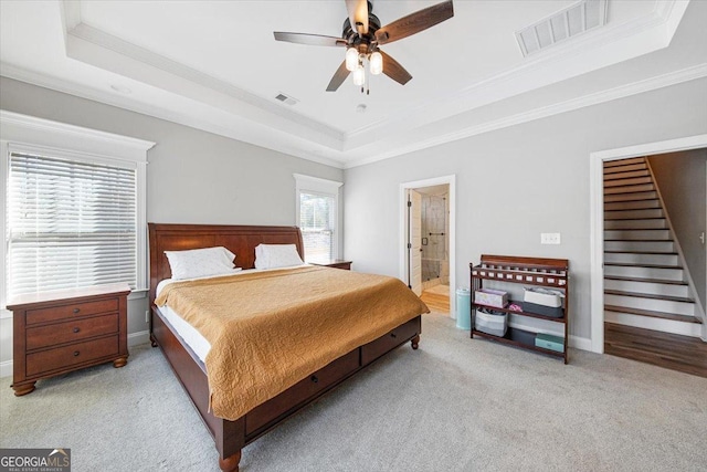 carpeted bedroom featuring a raised ceiling, ornamental molding, ceiling fan, and ensuite bath