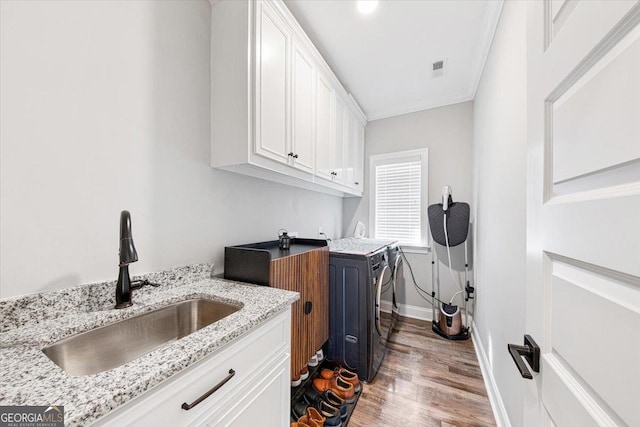 washroom featuring cabinet space, baseboards, light wood-style flooring, washing machine and clothes dryer, and a sink