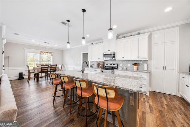 kitchen with stainless steel appliances, white cabinets, decorative light fixtures, and a spacious island