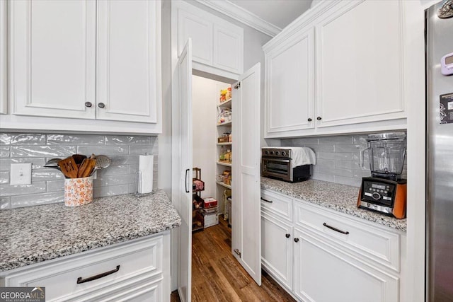 kitchen with light stone countertops, wood finished floors, white cabinets, ornamental molding, and decorative backsplash