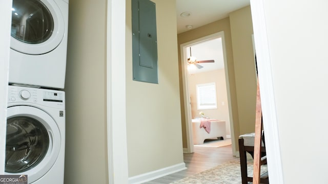 laundry room with hardwood / wood-style flooring, stacked washing maching and dryer, electric panel, and ceiling fan