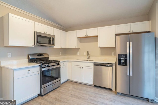 kitchen with stainless steel appliances, sink, white cabinets, and light hardwood / wood-style flooring