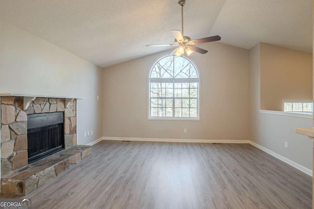 unfurnished living room featuring wood-type flooring, a stone fireplace, lofted ceiling, and a textured ceiling