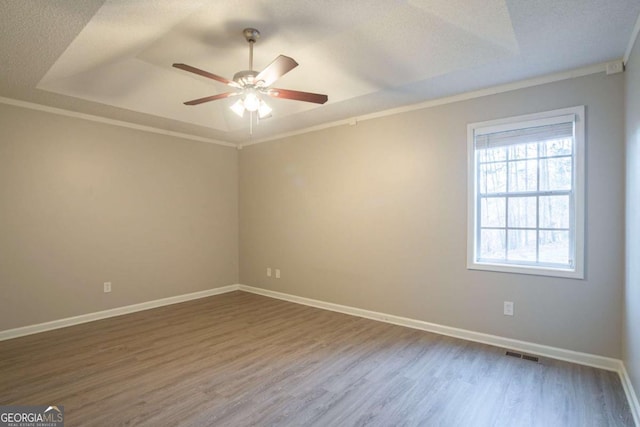 unfurnished room featuring crown molding, wood-type flooring, a raised ceiling, and a textured ceiling