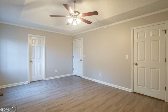 unfurnished bedroom with a raised ceiling, crown molding, wood-type flooring, and ceiling fan