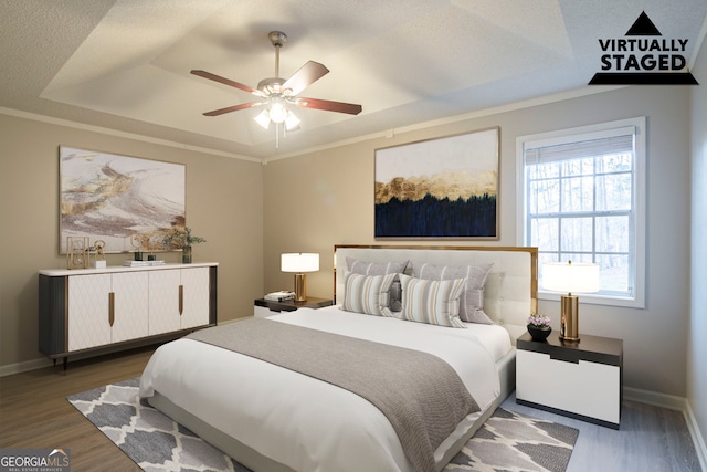 bedroom featuring dark hardwood / wood-style flooring, ornamental molding, a raised ceiling, and ceiling fan