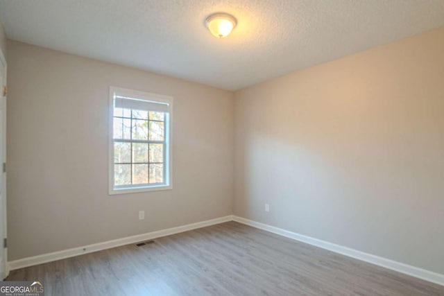 spare room with a textured ceiling and light hardwood / wood-style flooring