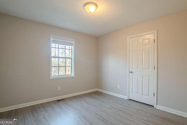 spare room with a textured ceiling and light hardwood / wood-style floors