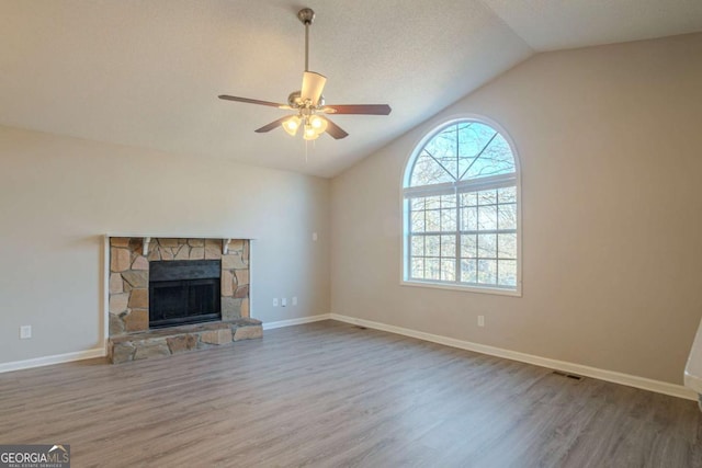 unfurnished living room featuring lofted ceiling, ceiling fan, wood-type flooring, a textured ceiling, and a stone fireplace