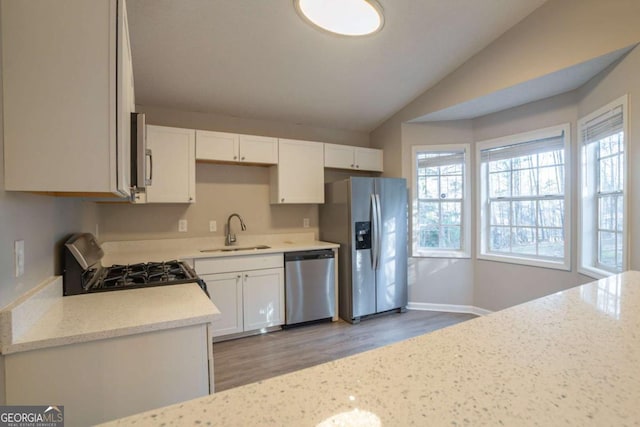 kitchen with appliances with stainless steel finishes, lofted ceiling, sink, white cabinets, and light stone countertops