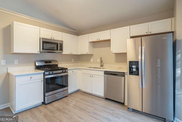 kitchen with appliances with stainless steel finishes, sink, white cabinets, and light hardwood / wood-style flooring