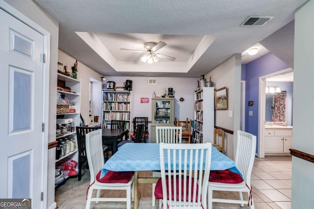 dining space with a raised ceiling, ceiling fan, light tile patterned floors, and a textured ceiling