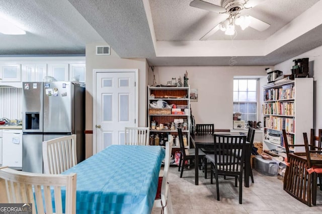 dining space with light tile patterned floors, a raised ceiling, a textured ceiling, and ceiling fan