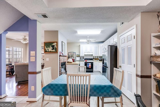 dining area featuring a textured ceiling, a fireplace, ceiling fan, and light tile patterned flooring