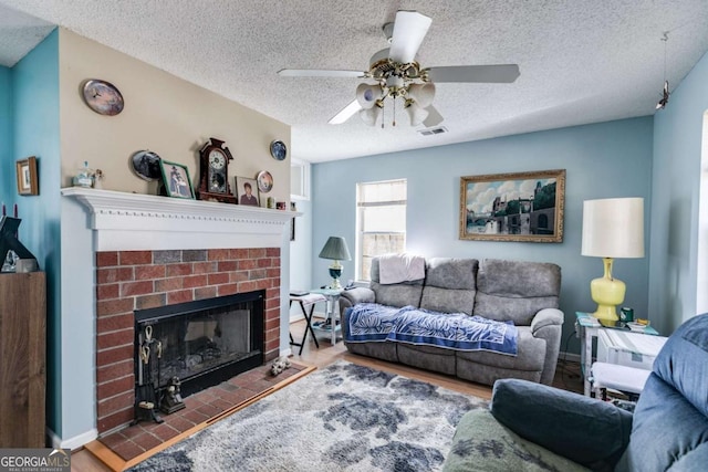 living room featuring ceiling fan, hardwood / wood-style floors, a brick fireplace, and a textured ceiling