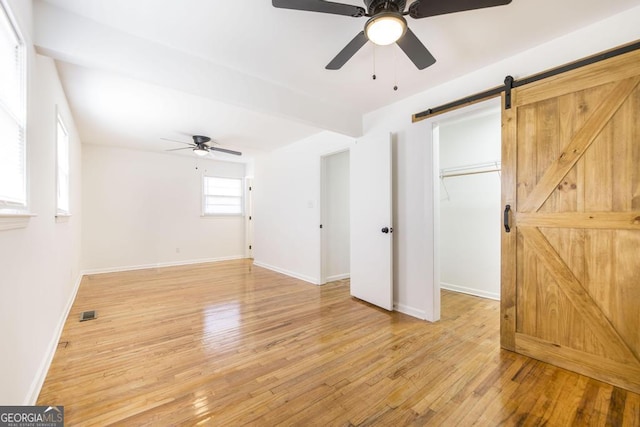 interior space featuring a spacious closet, light hardwood / wood-style flooring, a barn door, and ceiling fan