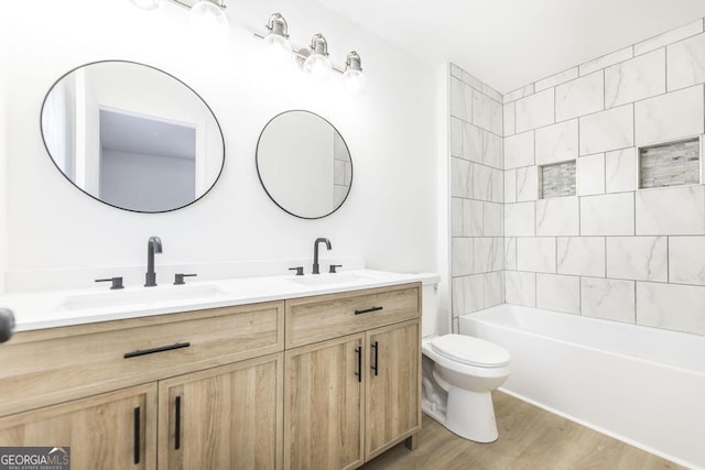 full bathroom with hardwood / wood-style flooring, tiled shower / bath, vanity, and toilet