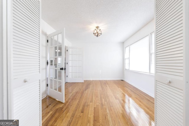 empty room with french doors, light hardwood / wood-style floors, and a textured ceiling