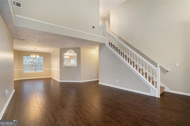 unfurnished living room featuring an inviting chandelier, a towering ceiling, and dark hardwood / wood-style flooring