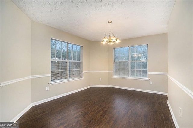 empty room featuring dark wood-type flooring, an inviting chandelier, and a textured ceiling