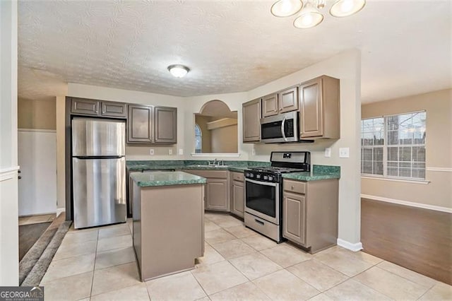 kitchen featuring light tile patterned floors, sink, stainless steel appliances, a center island, and a textured ceiling