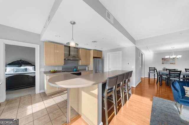 kitchen with a breakfast bar area, hanging light fixtures, a kitchen island, high end refrigerator, and wall chimney exhaust hood