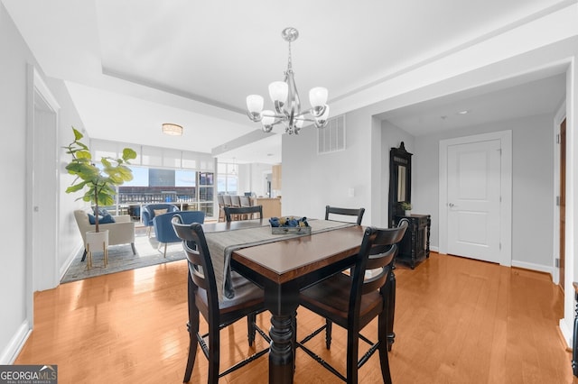 dining area with a notable chandelier, a raised ceiling, and light wood-type flooring