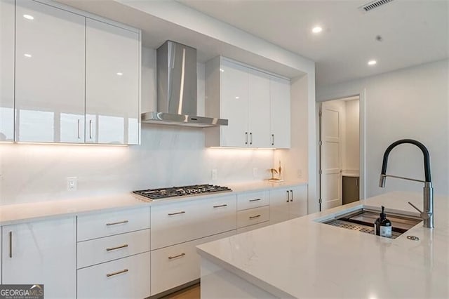 kitchen with wall chimney exhaust hood, sink, white cabinetry, tasteful backsplash, and stainless steel gas stovetop